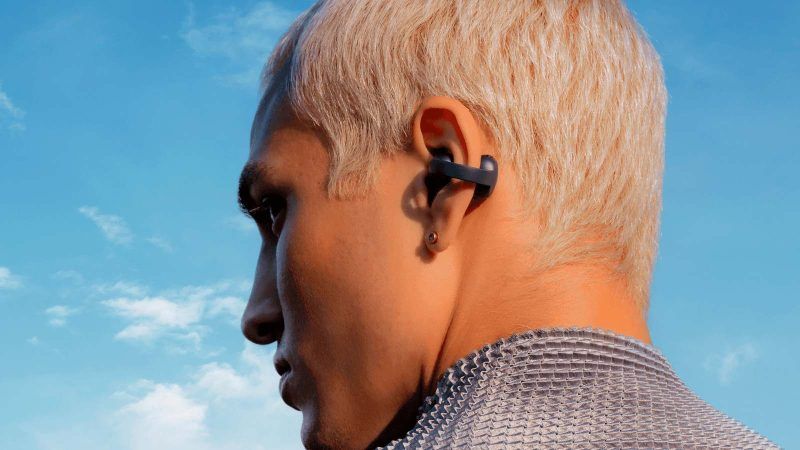Persona de perfil con auriculares de clip en la oreja y cielo azul de fondo.