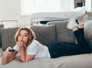 Mujer aburrida con control remoto viendo televisión en casa en autoaislamiento