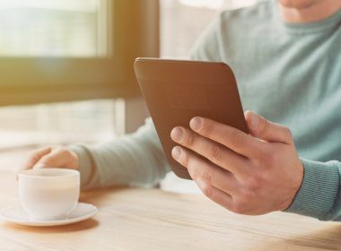 vista recortada del hombre estudiando con libro electrónico y sosteniendo una taza de té en casa