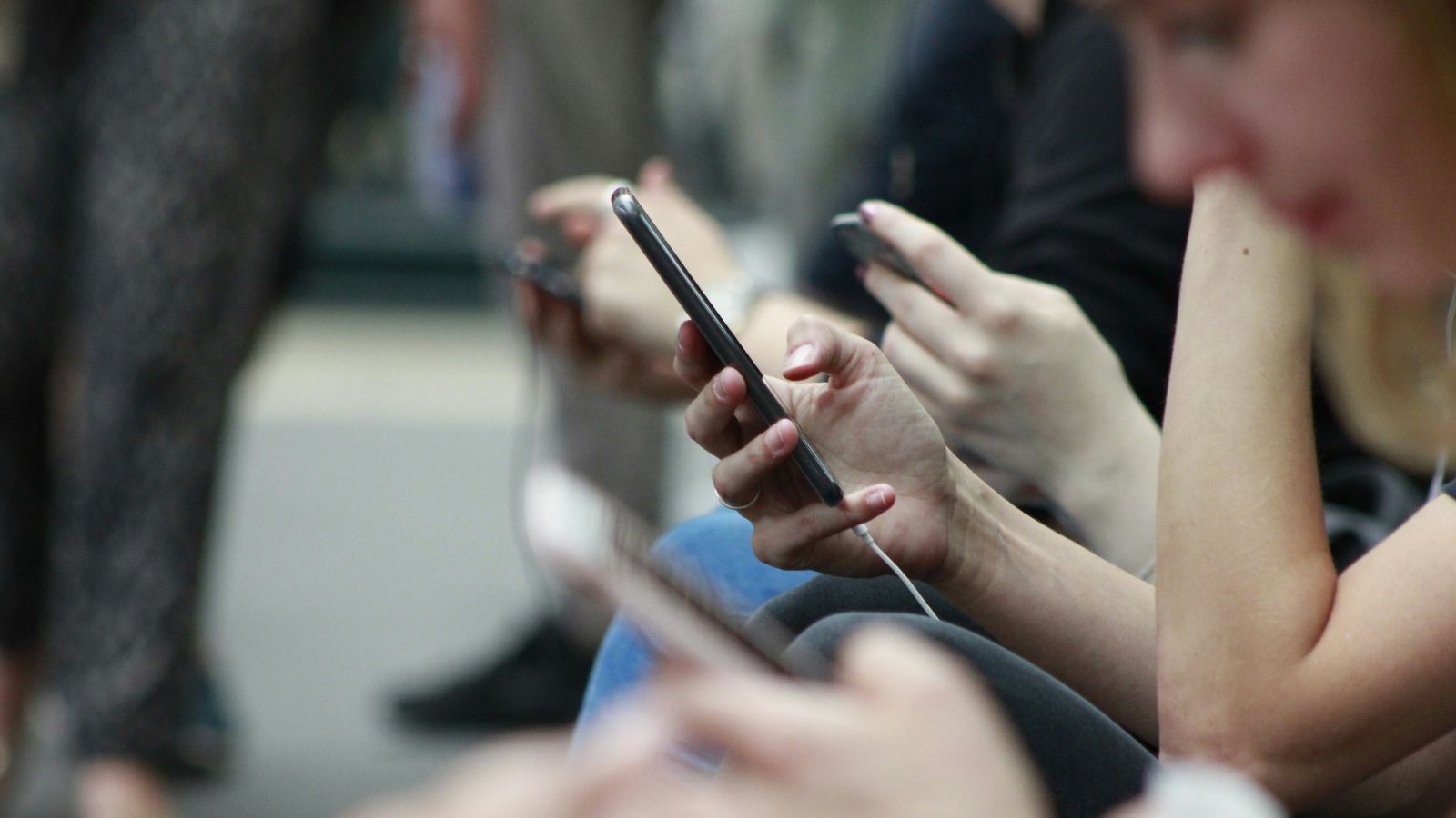 Primer plano de varias personas sentadas utilizando sus teléfonos móviles en un espacio público.