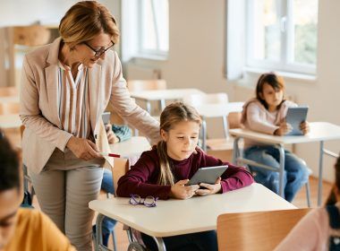 La colegiala utiliza el panel táctil con la ayuda del profesor durante una clase en el aula.