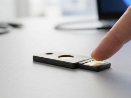 Dedo pulsando el sensor de una llave de seguridad física sobre una mesa.