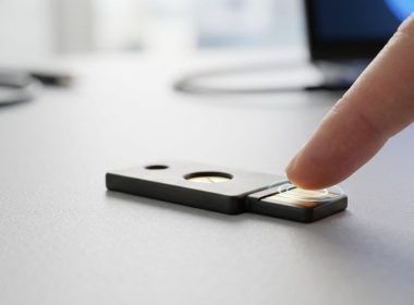 Dedo pulsando el sensor de una llave de seguridad física sobre una mesa.