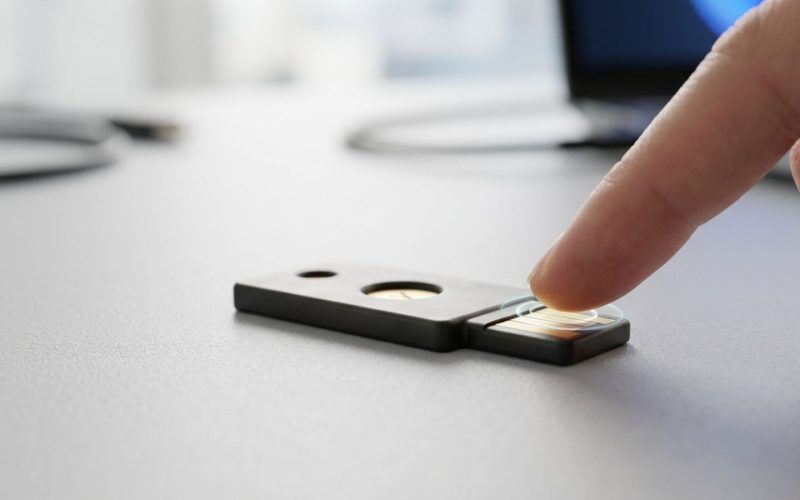 Dedo pulsando el sensor de una llave de seguridad física sobre una mesa.