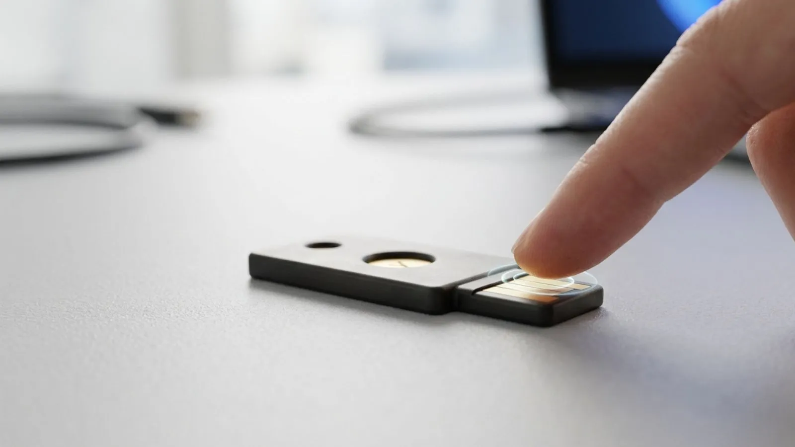 Dedo pulsando el sensor de una llave de seguridad física sobre una mesa.