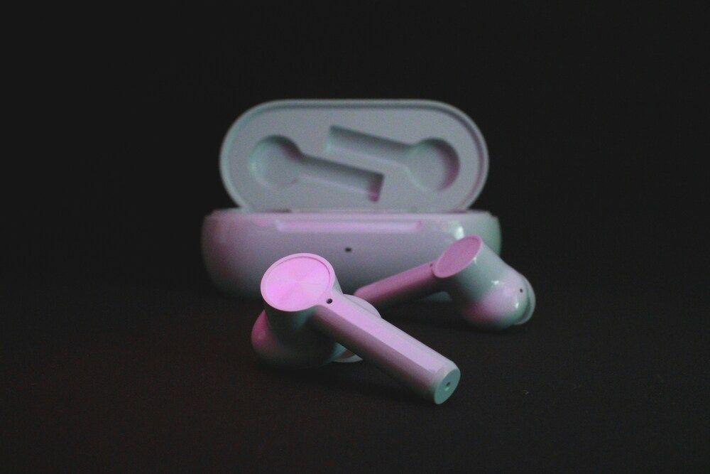 Auriculares inalámbricos de tipo bastón junto a su estuche de carga abierto sobre un fondo oscuro.