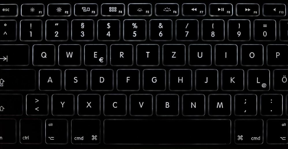 Primer plano de un teclado retroiluminado en un entorno oscuro con las teclas resaltadas por una luz blanca tenue.