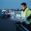 Agente de policía consultando una interfaz digital holográfica con datos de un vehículo y conductor durante un control nocturno en carretera.