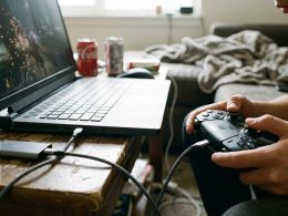 Primer plano de un jugador utilizando un mando conectado por cable a un ordenador portátil gaming en un salón.