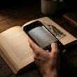 Mano sosteniendo un teléfono móvil para escanear y traducir el texto de un libro antiguo sobre una mesa de madera.