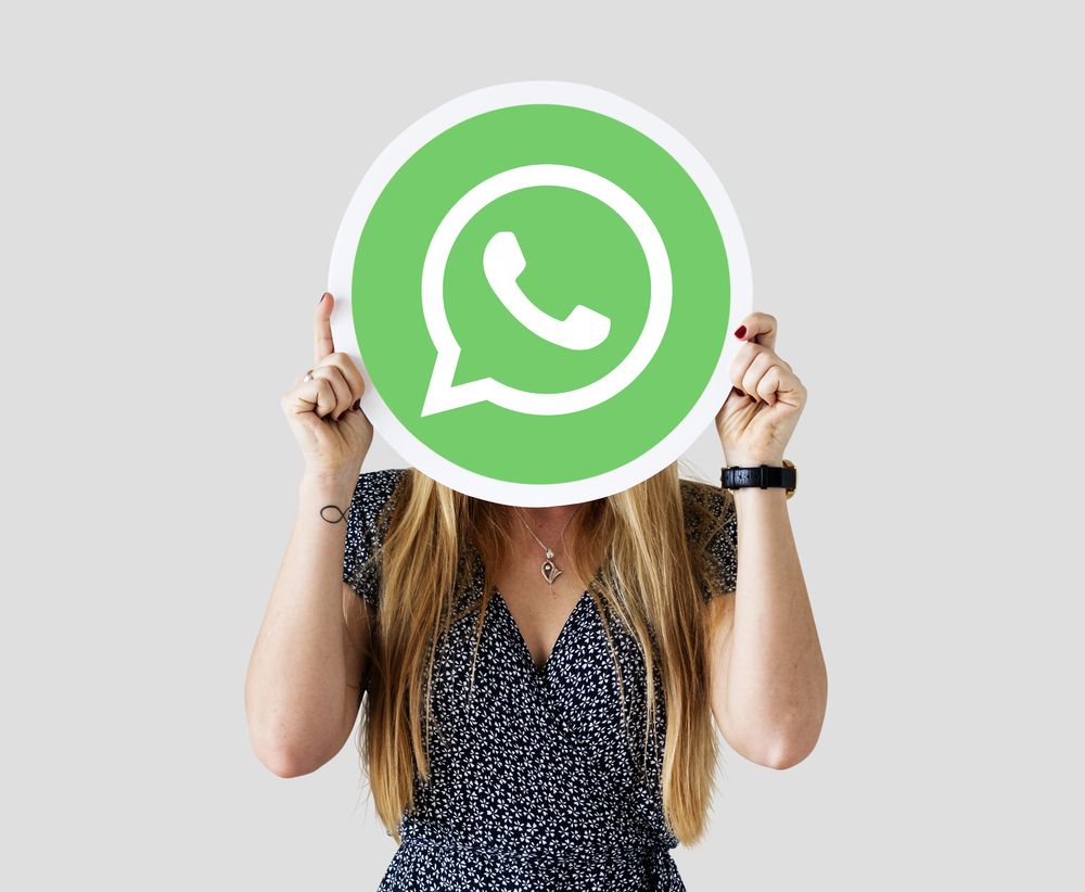 Mujer sosteniendo un cartel circular con el logotipo de WhatsApp frente a su rostro.