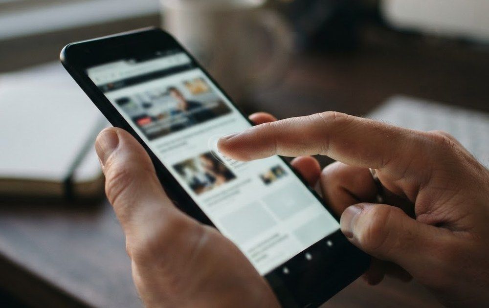 Primer plano de unas manos utilizando un teléfono inteligente para navegar por una página web con artículos y vídeos.