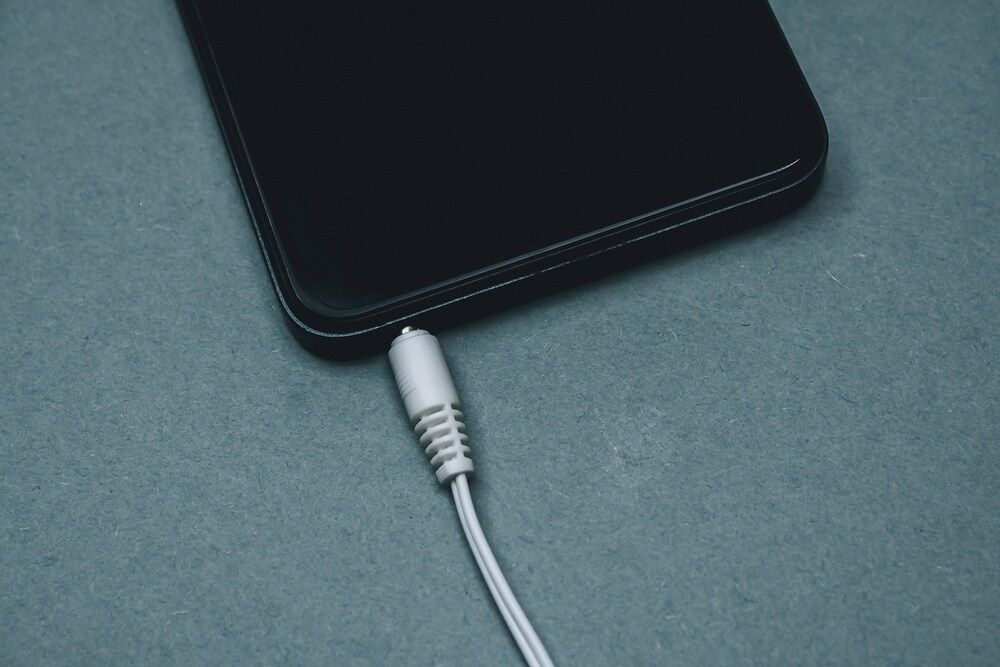 Primer plano del borde inferior de un smartphone con un cable blanco conectado al puerto de carga.