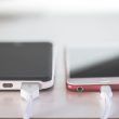 Dos teléfonos inteligentes conectados a cables de carga sobre una superficie clara.