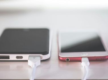 Dos teléfonos inteligentes conectados a cables de carga sobre una superficie clara.