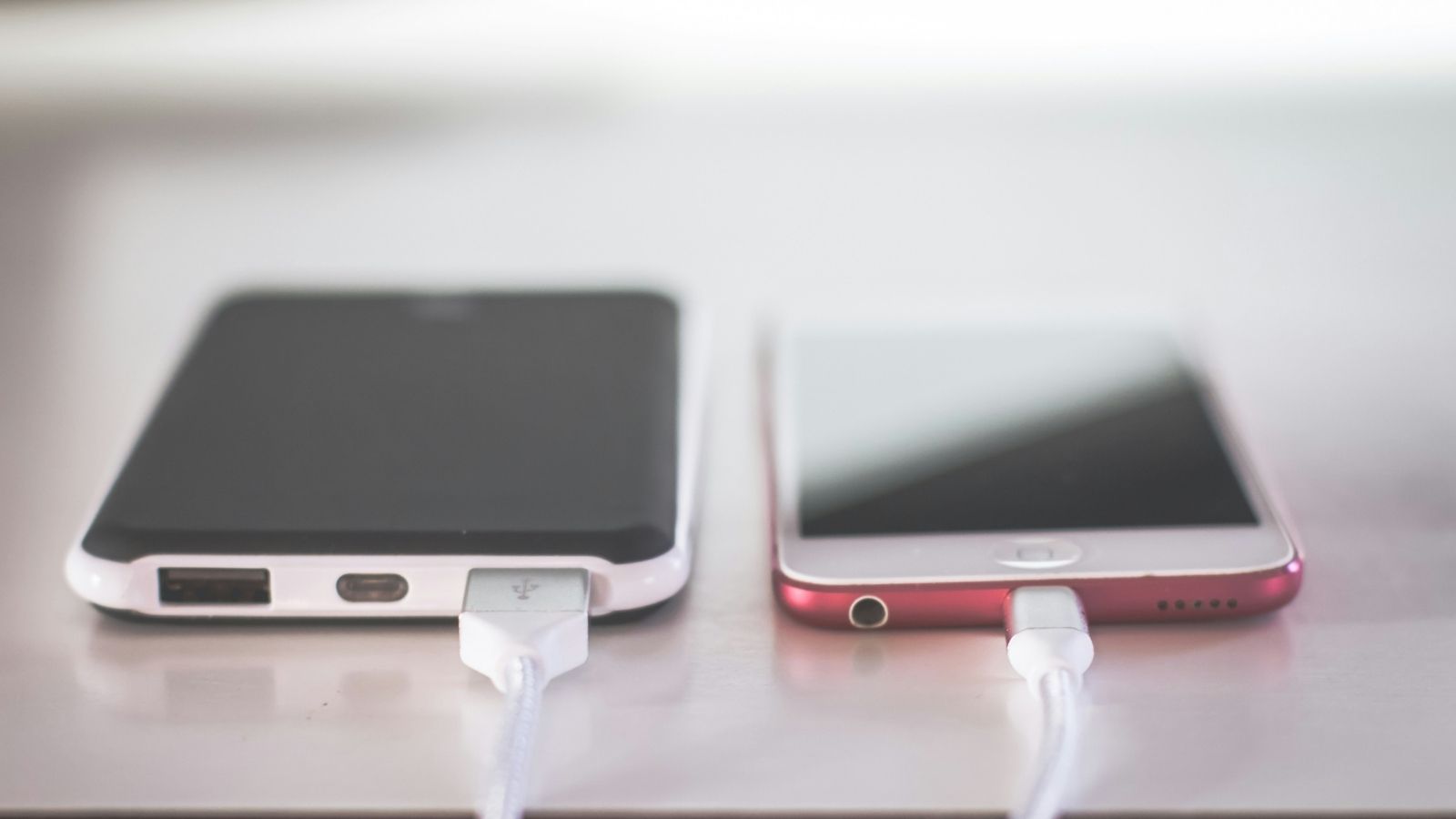 Dos teléfonos inteligentes conectados a cables de carga sobre una superficie clara.