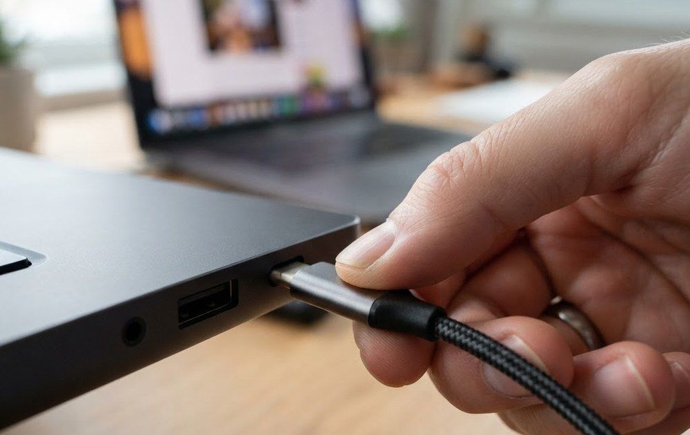 Primer plano de una mano introduciendo un conector USB-C en el puerto lateral de un ordenador portátil.