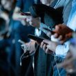 Primer plano de varias personas utilizando sus teléfonos inteligentes en un evento nocturno con iluminación azulada.