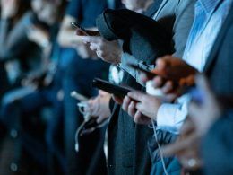 Primer plano de varias personas utilizando sus teléfonos inteligentes en un evento nocturno con iluminación azulada.