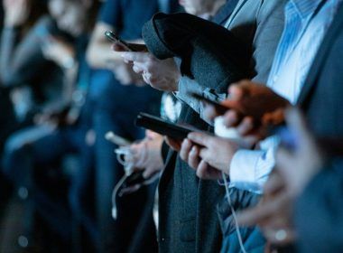 Primer plano de varias personas utilizando sus teléfonos inteligentes en un evento nocturno con iluminación azulada.