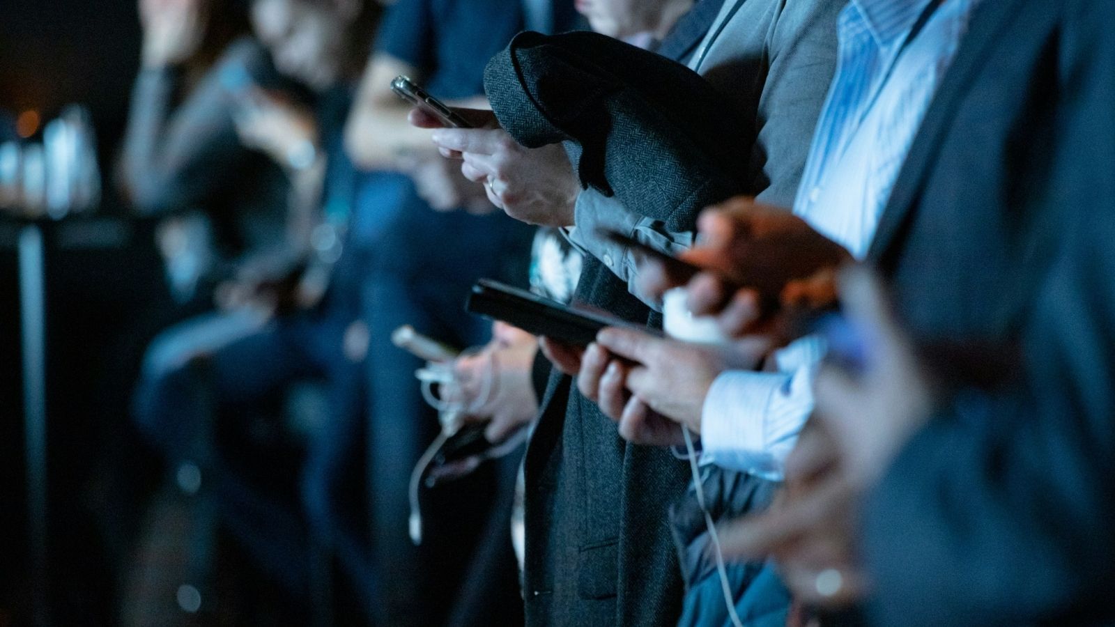 Primer plano de varias personas utilizando sus teléfonos inteligentes en un evento nocturno con iluminación azulada.