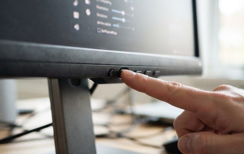 Primer plano de un dedo pulsando un botón físico en el borde inferior de un monitor de ordenador.