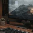 Monitor de ordenador en un escritorio de madera mostrando un paisaje de montaña en escala de grises.