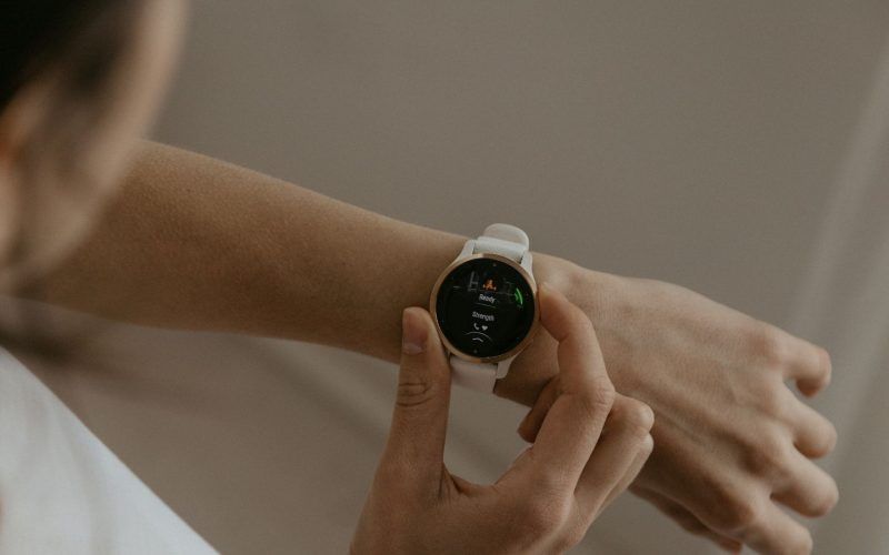 Primer plano de una persona consultando su frecuencia cardíaca en la pantalla de un reloj inteligente con correa blanca.