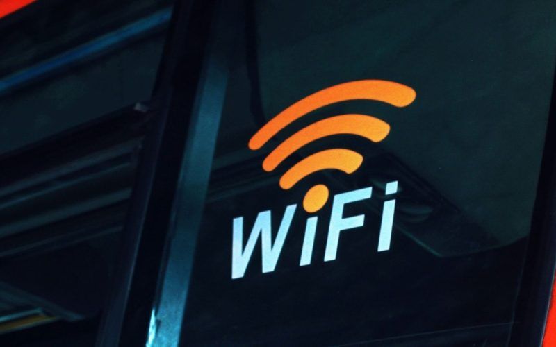 Pegatina con el símbolo de WiFi naranja y texto blanco sobre el cristal oscuro de un vehículo de transporte público.