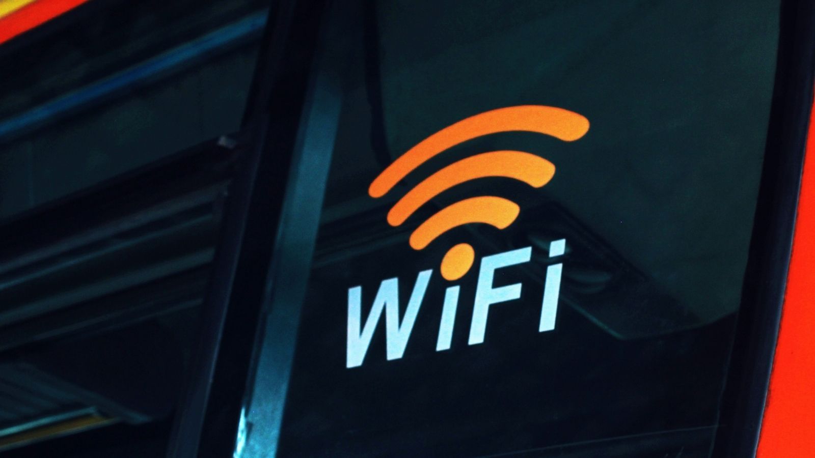 Pegatina con el símbolo de WiFi naranja y texto blanco sobre el cristal oscuro de un vehículo de transporte público.