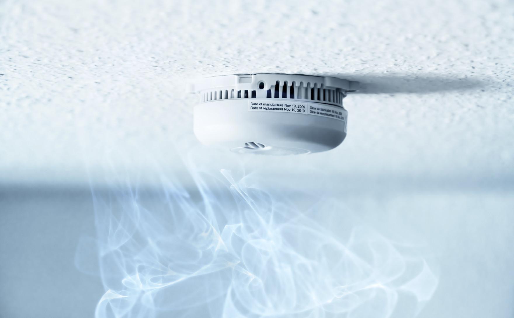 A smoke detector installed at a ceiling with smoke. Small depth of field.